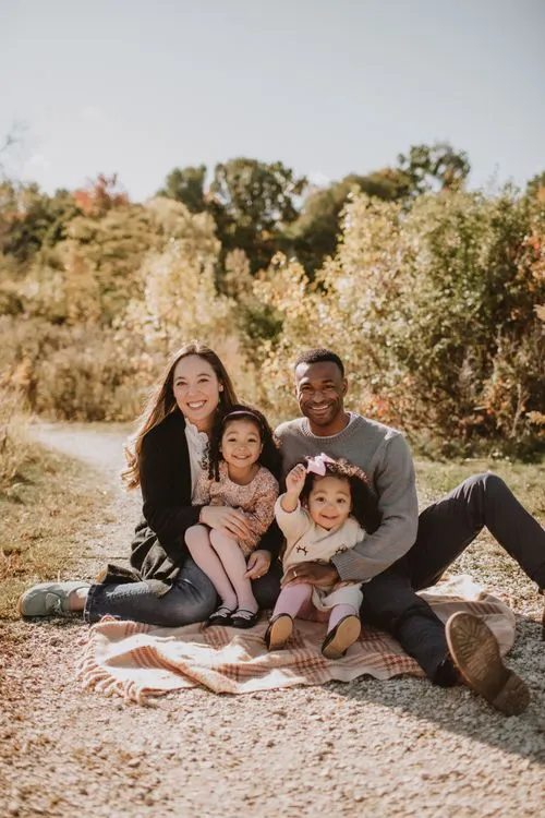 A family sitting on a blanket on a dirt road.
